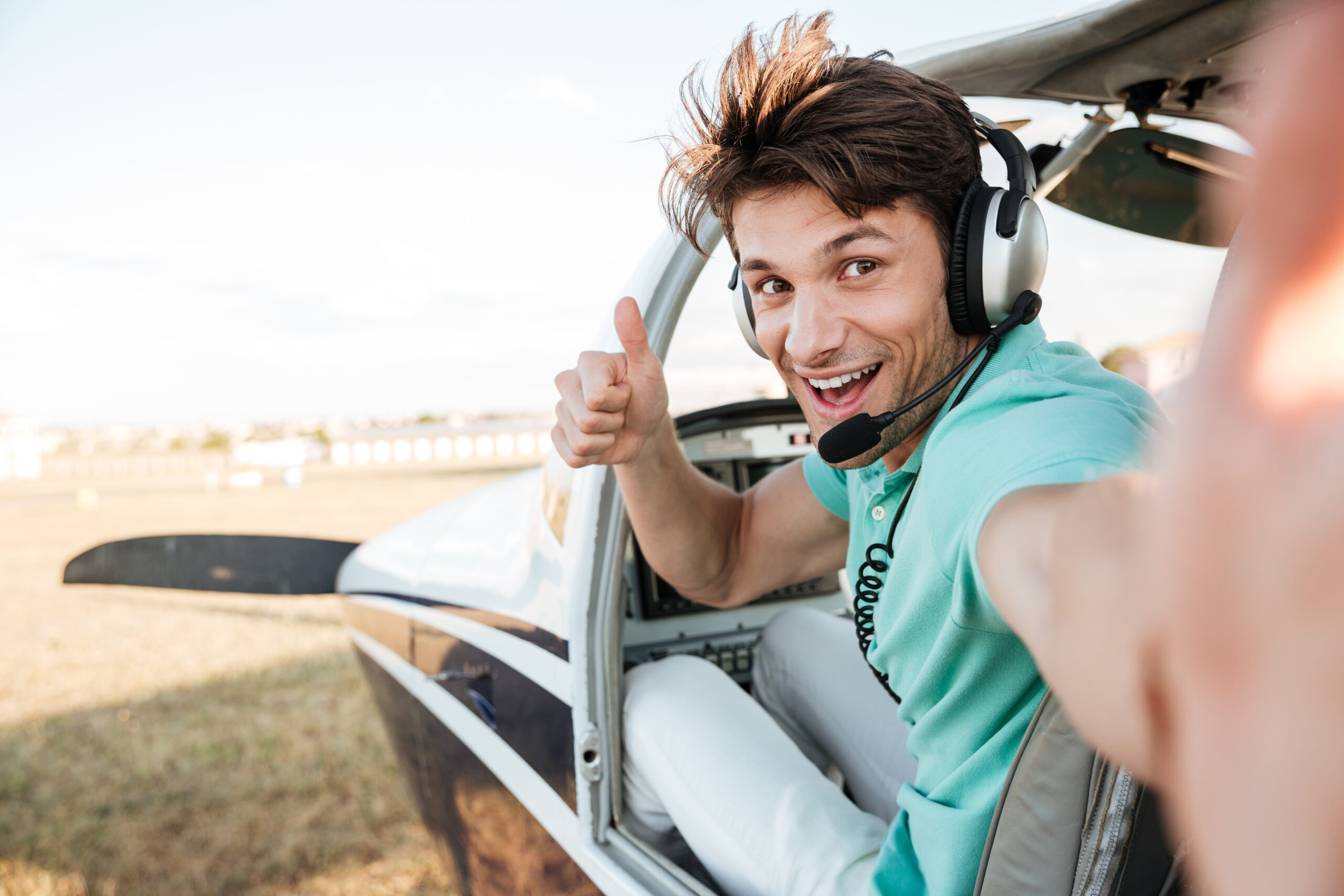 graphicstock cheerful excited young pilot sitting in cabin of small airplane and showing thumbs up Bu d7SuH2g scaled