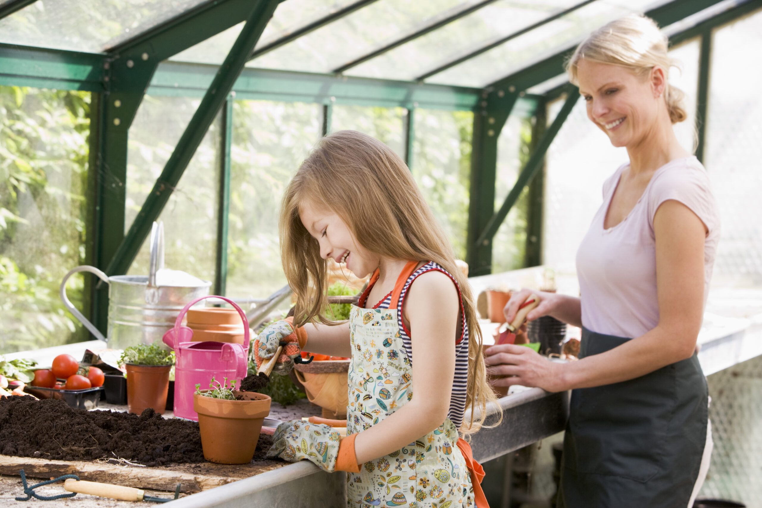 young girl and woman in greenhouse putting soil in pots smiling BKbeZtj0ri scaled